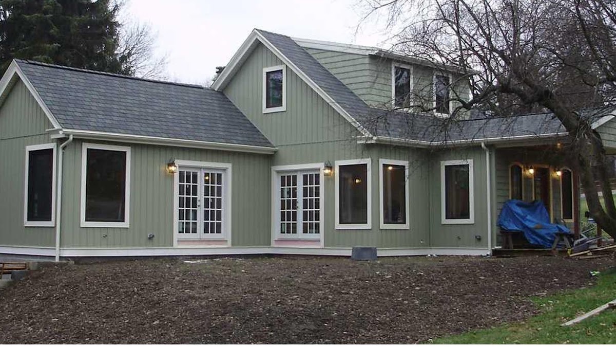 A home addition with new green vertical siding, new windows, and new roofing, mid-construction